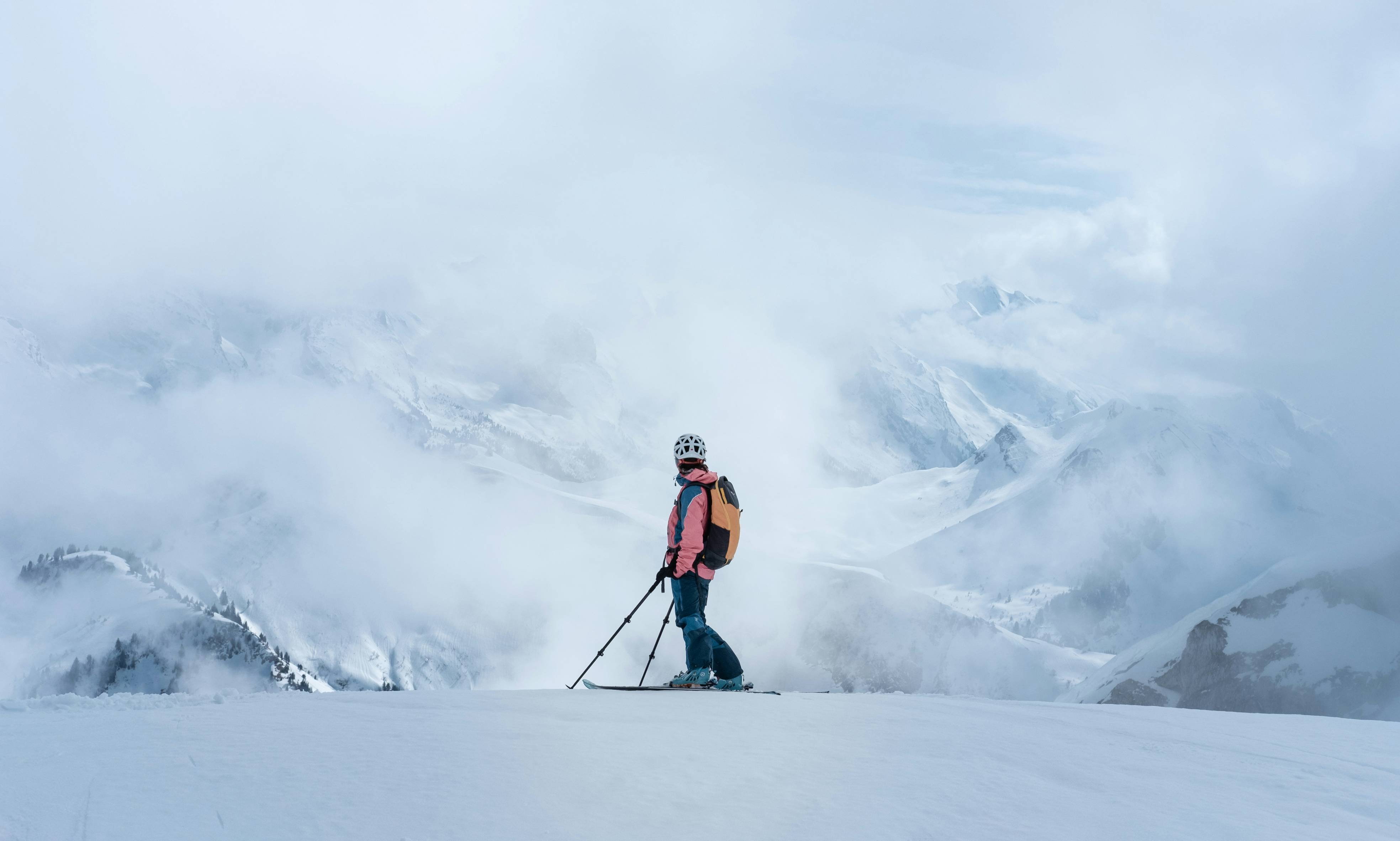 man in orange jacket and black pants standing on snow covered ground