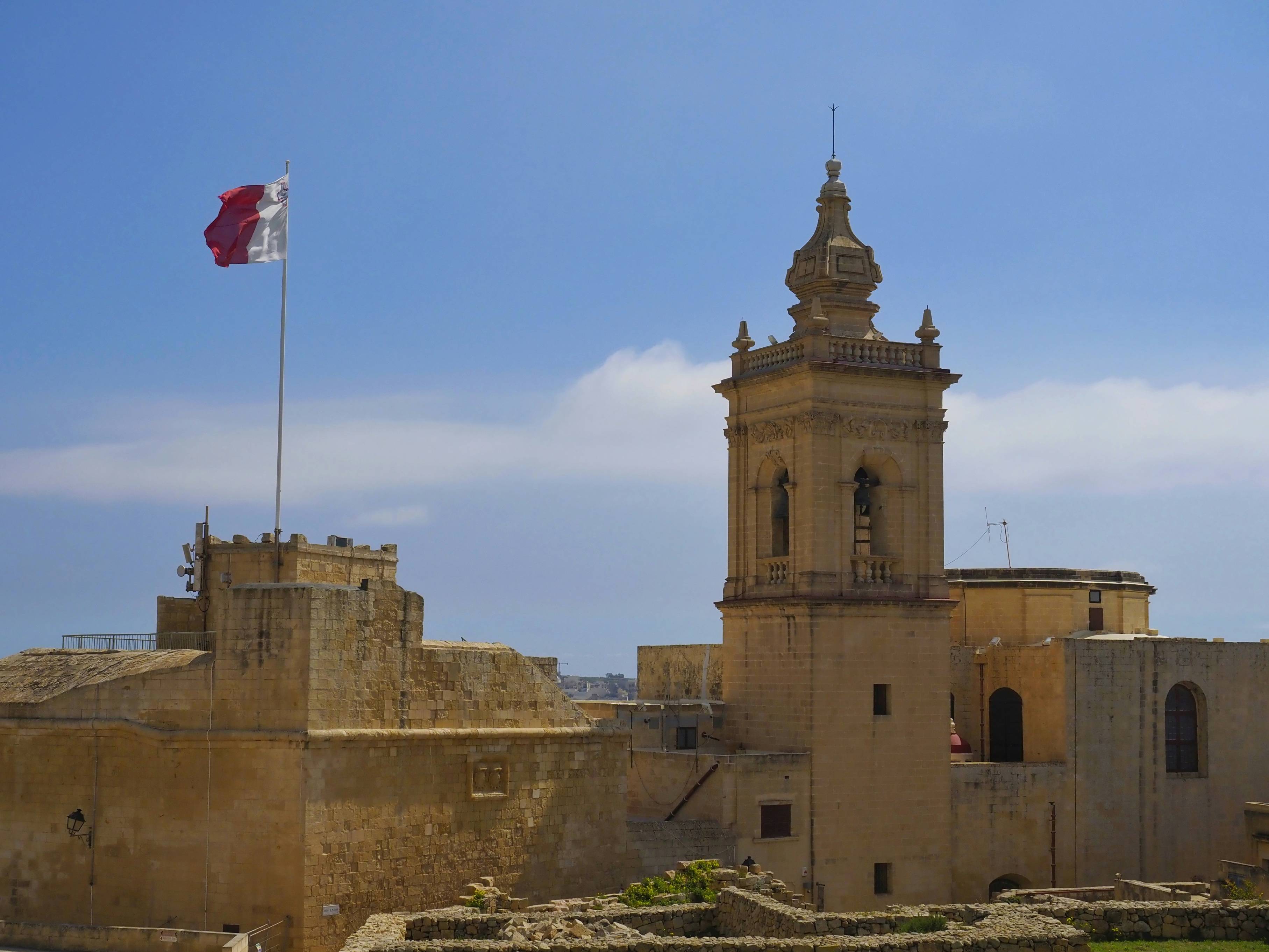 A castle flies a flag under a bright sky.